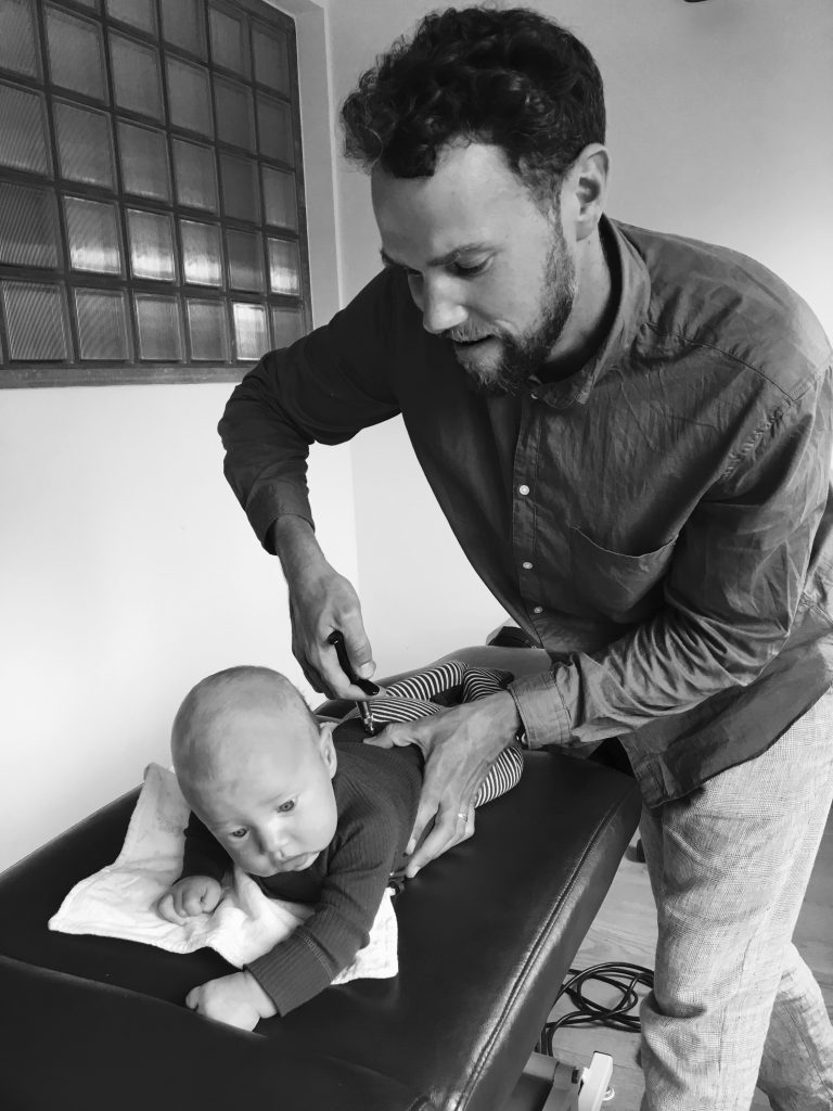 Chiropractor Andrew Harvey behandelt een baby met een zacht instrument